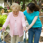 Senior woman struggles to walk with the help of a walker and her young granddaughter.